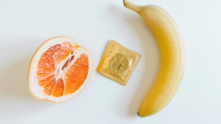 Half a grapefruit, a packaged condom, and a banana laid flat 